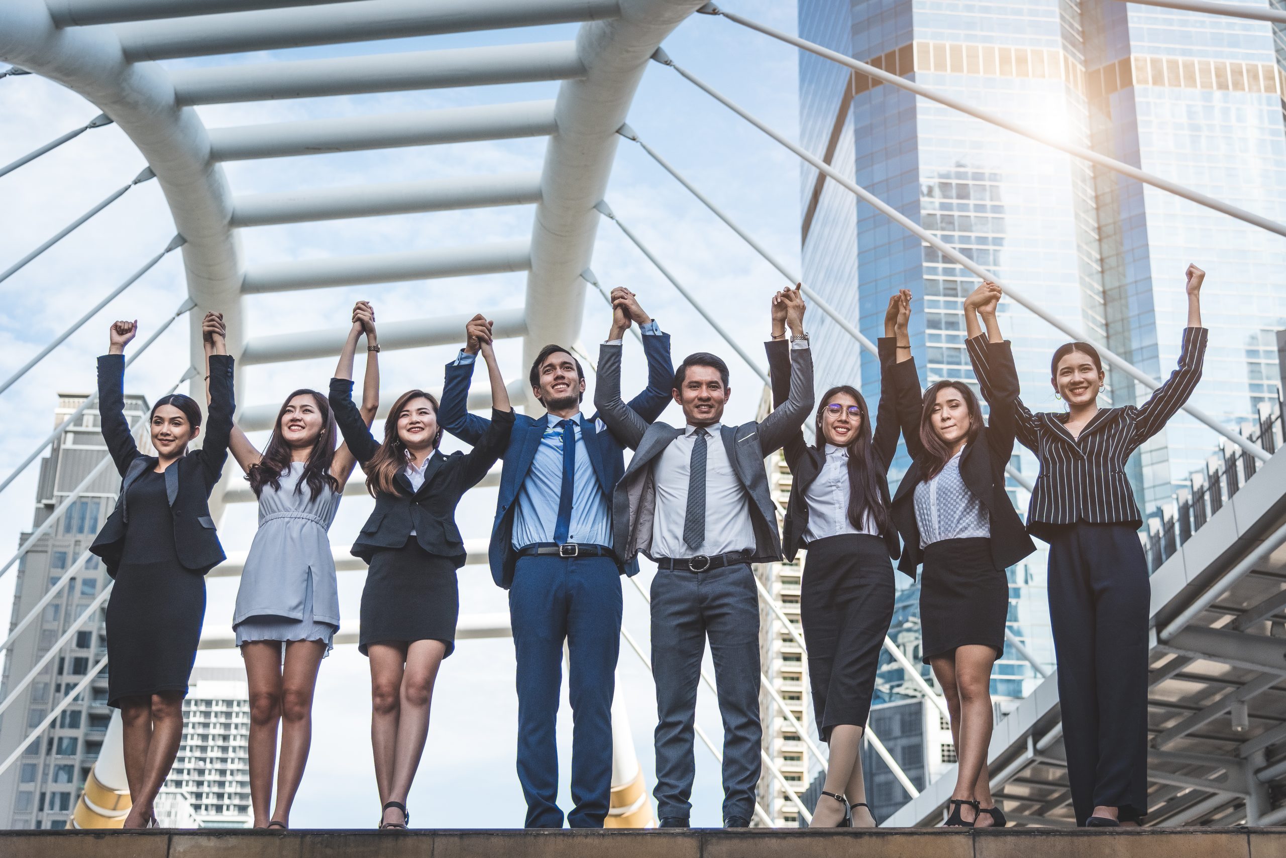 Group of young professionals holding hands in the air.